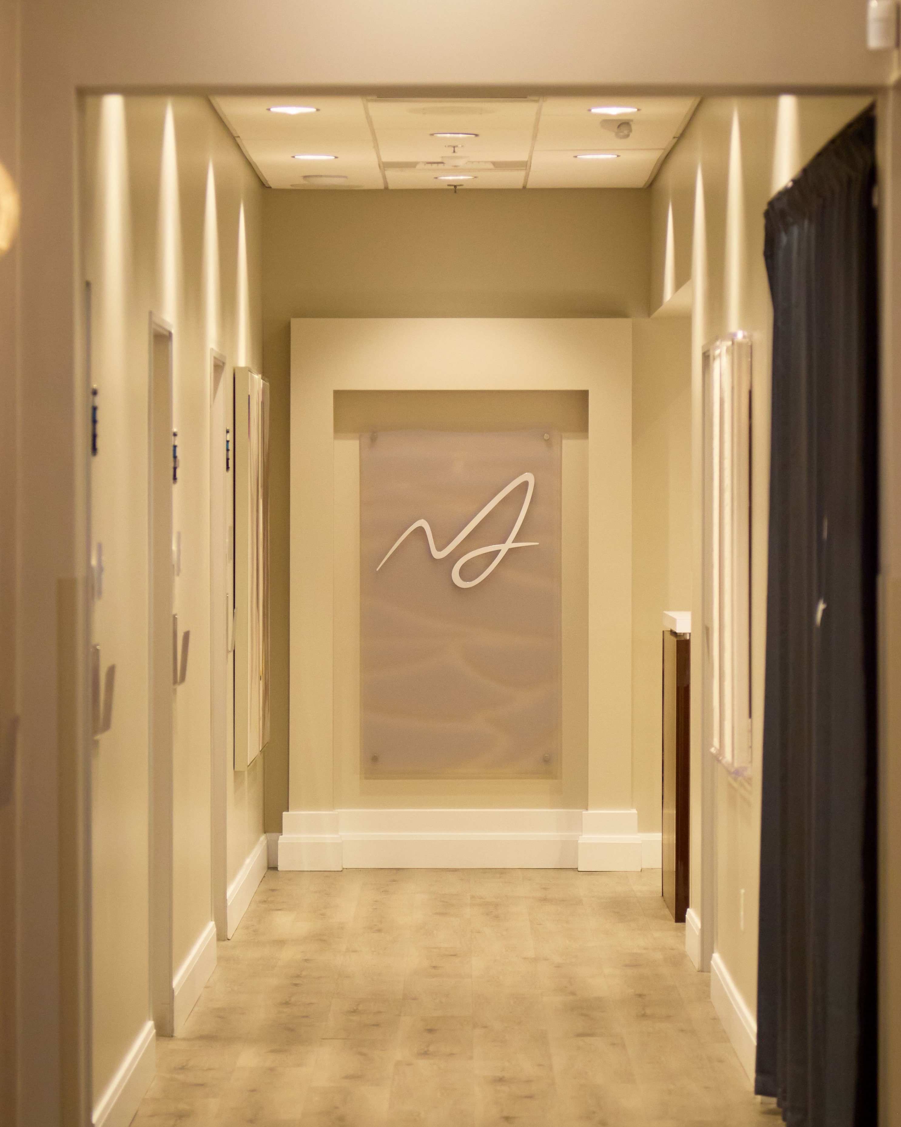 The warmly lit clinic hallway leading to the etched Macias Dermatology wordmark