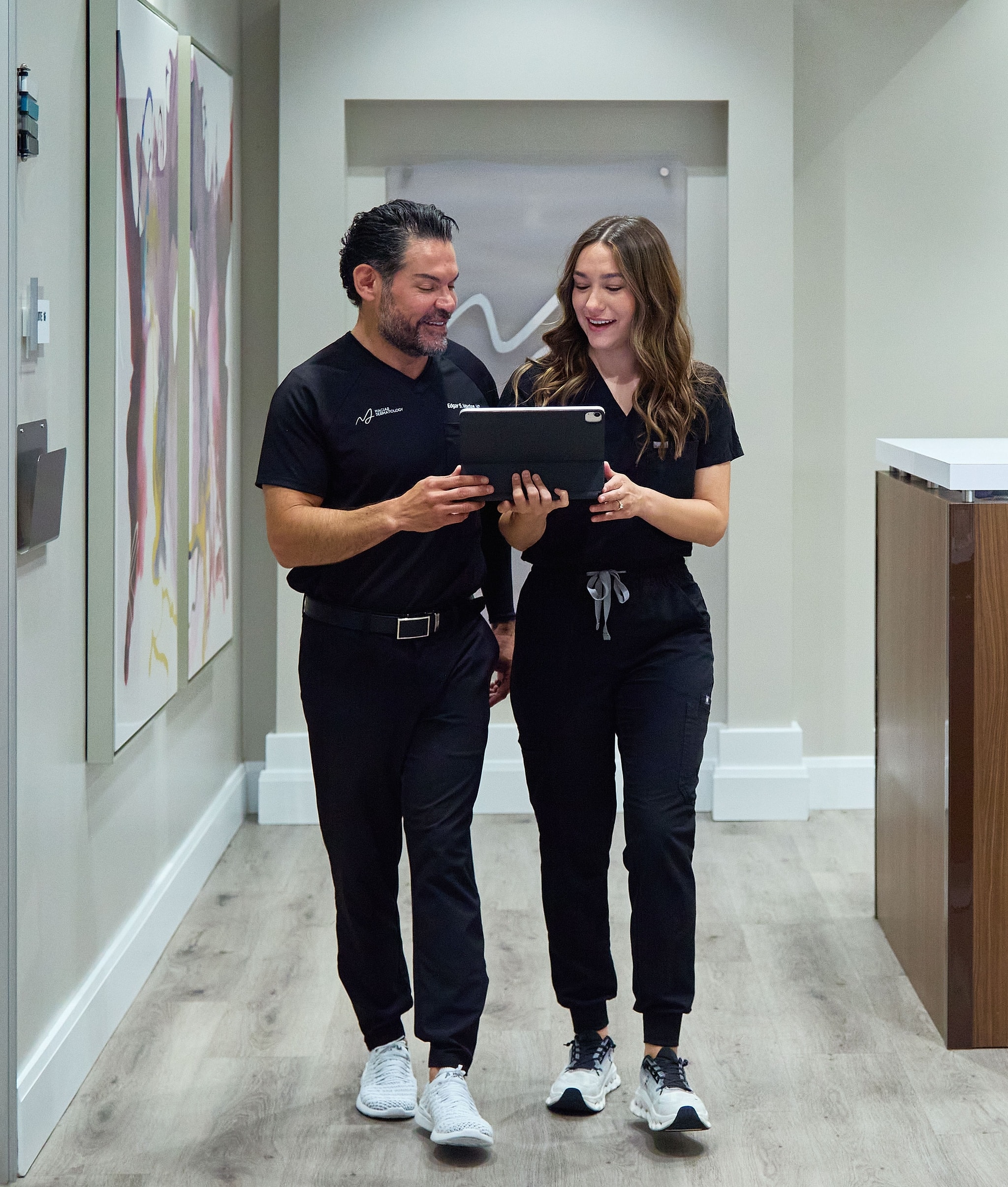 Dr. Edgar Macias and a Macias Dermatology team member walking the clinic hallway, reviewing notes together