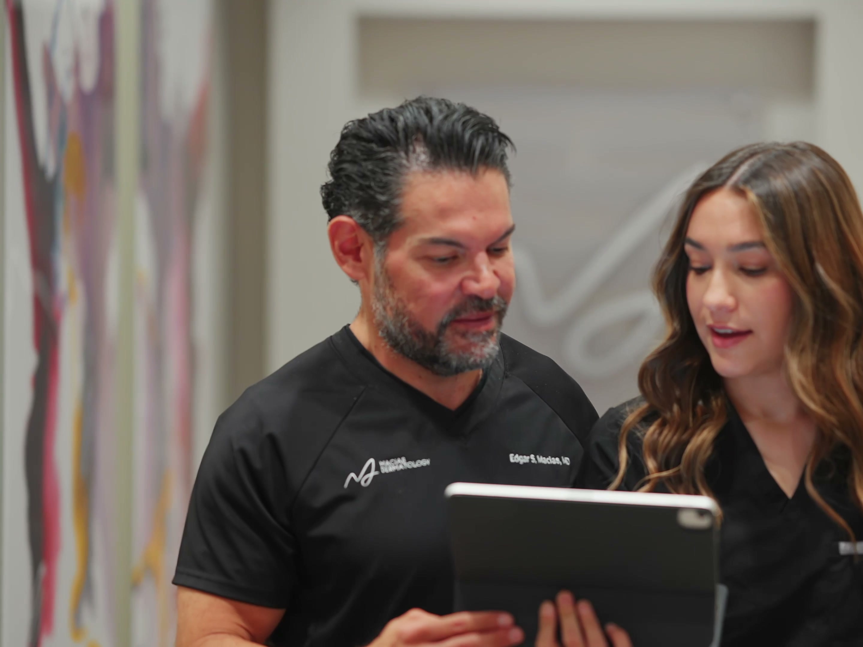 Dr. Macias and a physician assistant smiling over a tablet beneath the practice wordmark