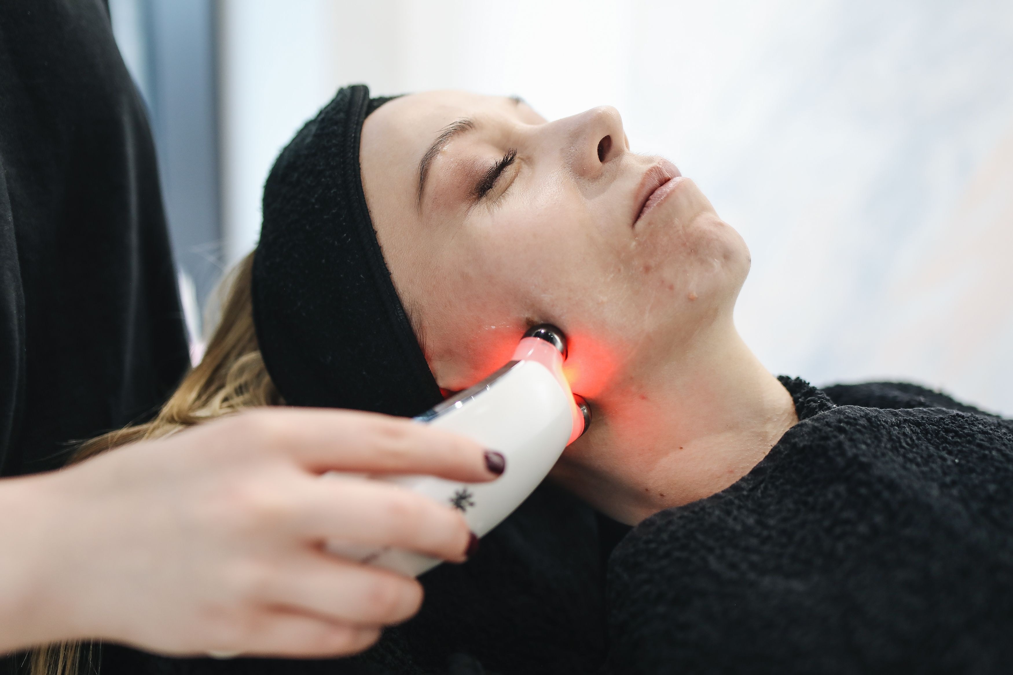 A treatment handpiece glowing red against a patient's cheek